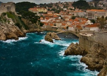 A view of the coast of Croatia with the orange roofed homes and blue ocean crashing against the rocky shores