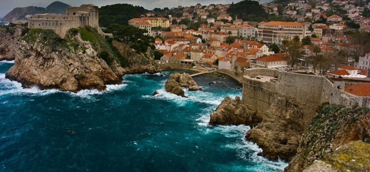 A view of the coast of Croatia with the orange roofed homes and blue ocean crashing against the rocky shores