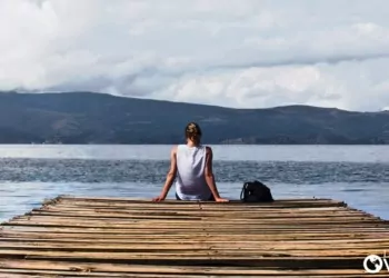 a woman with a backpack sitting at the end of a dock