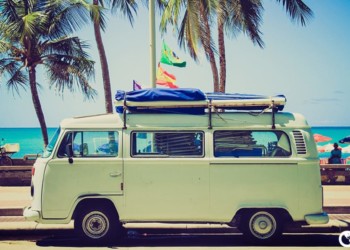 A van with surfboards strapped to the top parked in front of the beach. importing a truck to belize