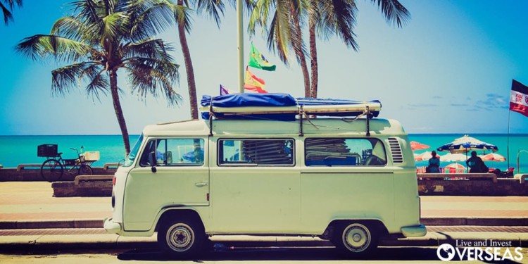 A van with surfboards strapped to the top parked in front of the beach. importing a truck to belize