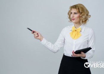 a blond woman wearing a white button down shirt and yellow bowtie holding a tablet