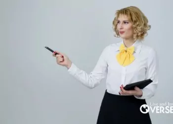 a blond woman wearing a white button down shirt and yellow bowtie holding a tablet