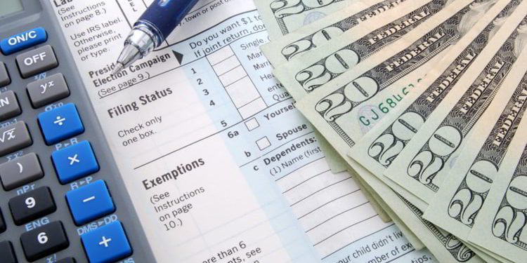 Forms to file U.S taxes, a calculator, a pen, and twenty dollar bills