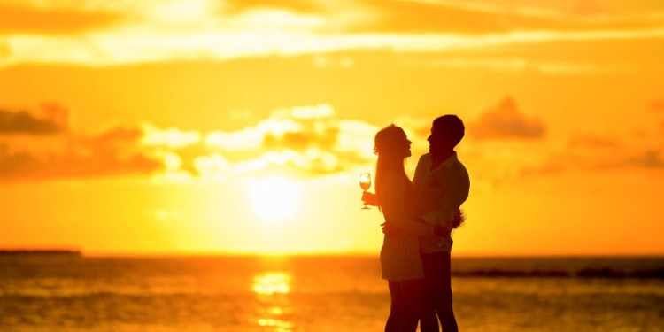 A couple on a honeymoon toasting with the sun shining over the water at dusk.