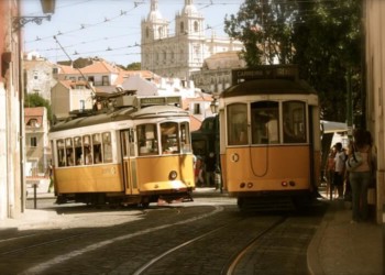 two old fashioned yellow trolley cabs travelling in front of a cathedral in porto, portugal