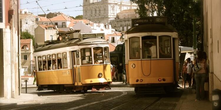 two old fashioned yellow trolley cabs travelling in front of a cathedral in porto, portugal
