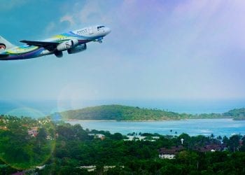 A bright striped plane landing over a lush and beautiful country below.