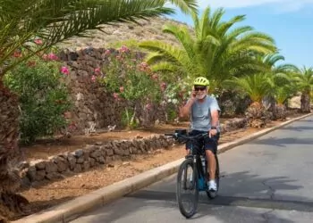 Senior man wearing sunglasses talking over smart phone while riding bicycle on road in park.