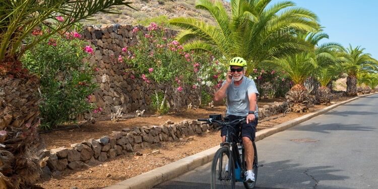 Senior man wearing sunglasses talking over smart phone while riding bicycle on road in park.