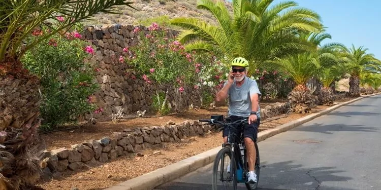 Senior man wearing sunglasses talking over smart phone while riding bicycle on road in park.