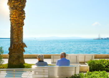 A mature couple sit on a bench and enjoy a view of the Adriatic Sea at the Riva Promenade on the Dalmatian Coast of Croatia.