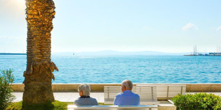 A mature couple sit on a bench and enjoy a view of the Adriatic Sea at the Riva Promenade on the Dalmatian Coast of Croatia.