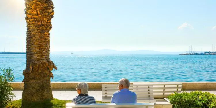 A mature couple sit on a bench and enjoy a view of the Adriatic Sea at the Riva Promenade on the Dalmatian Coast of Croatia.