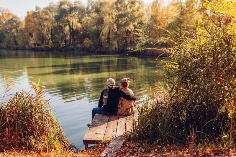 Senior family couple relaxing by autumn lake.