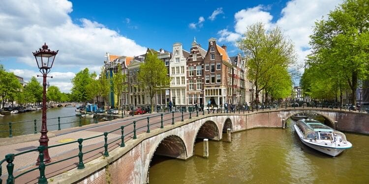 Beautiful Amsterdam Canal with buildings in the background and a boat on the water.
