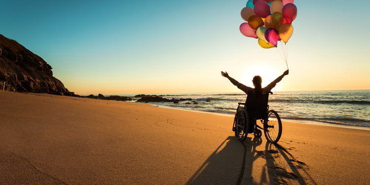 A person on a wheelchair with colorful balloons at the beach