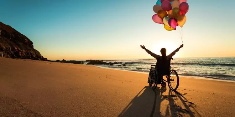 A person on a wheelchair with colorful balloons at the beach