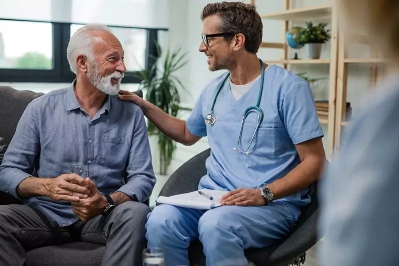 Happy doctor talking to senior male patient while being in a home visit