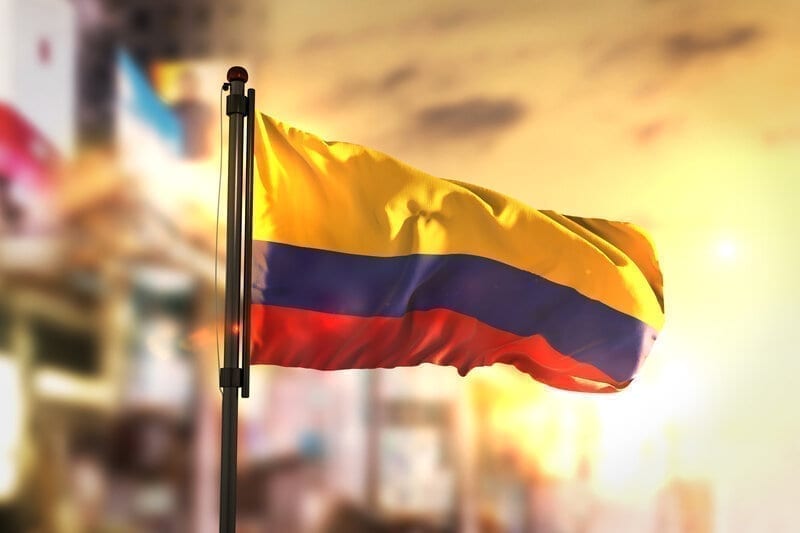 Colombia Flag Against City Blurred Background At Sunrise Backlight