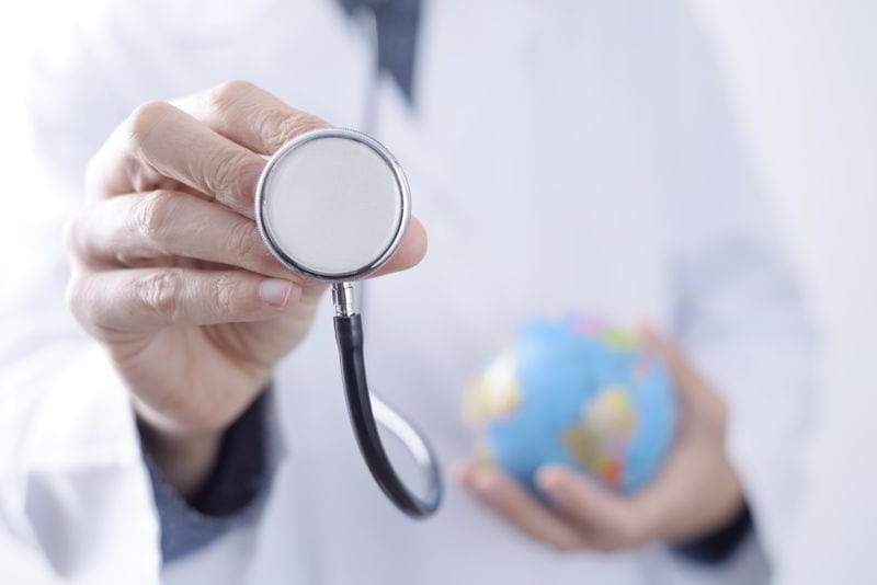 Closeup of a young caucasian doctor man with a world globe in one hand and a stethoscope in the other hand.