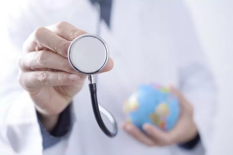 Closeup of a young caucasian doctor man with a world globe in one hand and a stethoscope in the other hand.