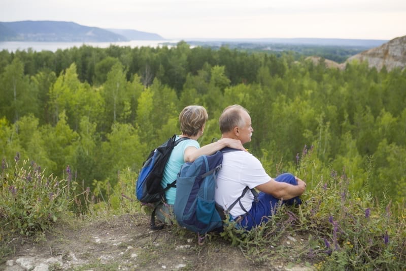 retired couple with backpacks sits on the mountain.