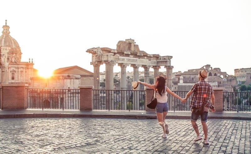 Young couple tourist walking pointing towards Roman Forum at sunrise, Italy.
