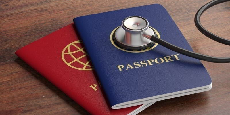 Travelling for health, medical tourism. Blue and red passports and stethoscope on wooden background.