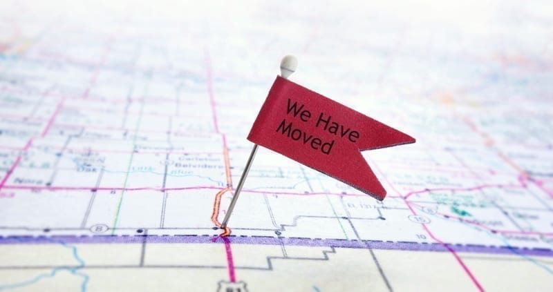 Closeup of red pin flag on a map with We Have Moved text