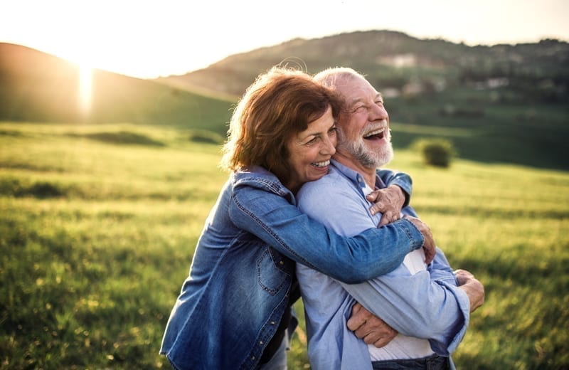 Happy senior couple outside in spring nature, hugging at sunset.