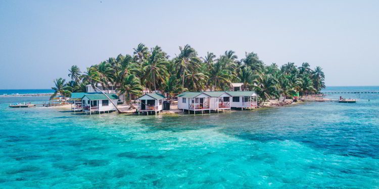View of Tobacco Caye small Caribbean island with palm trees and bungalows in the Belize Barrier Reef