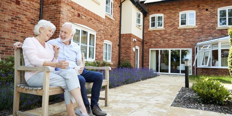 Retired couple sitting on bench with hot drink in assisted living facility
