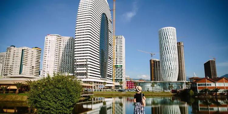Tourist girl in a hat and with a backpack on the background of modern high-rise buildings in Batumi, Adjara, Georgia.