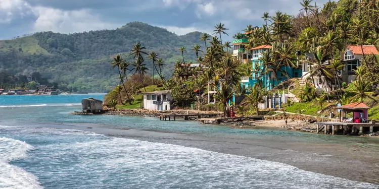 Palm trees, sea and houses in Isla Grande shore. Colon province, Panama 