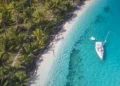 A white sailing yacht anchoring in crystal clear turquoise water right next to a paradisiacal island in San Blas, Panama