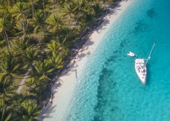 A white sailing yacht anchoring in crystal clear turquoise water right next to a paradisiacal island in San Blas, Panama