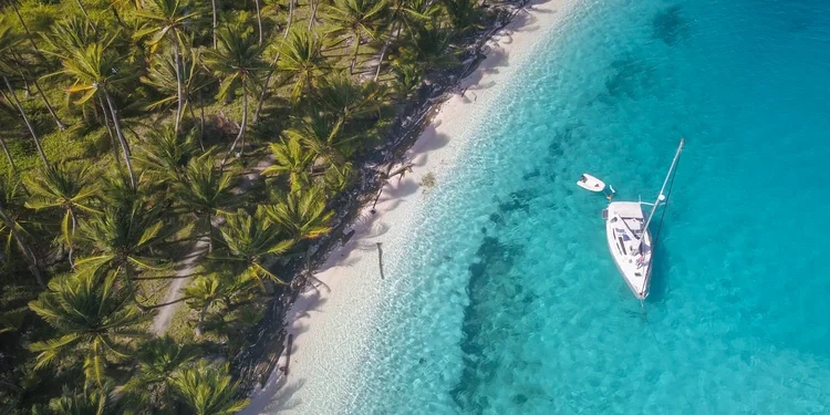 A white sailing yacht anchoring in crystal clear turquoise water right next to a paradisiacal island in San Blas, Panama
